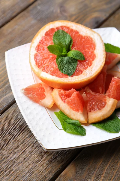 Zralé nasekané grapefruitu s mátou listy na talíř, na dřevěné pozadí — Stock fotografie