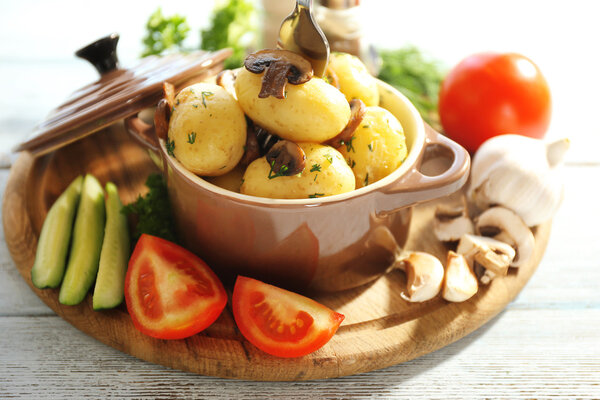 Young boiled potatoes in pan with vegetables on table in kitchen