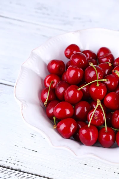 Sweet cherries in color bowl on wooden background — Stock Photo, Image