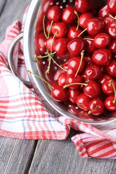 Sweet cherries in colander on color wooden background — Stock Photo, Image