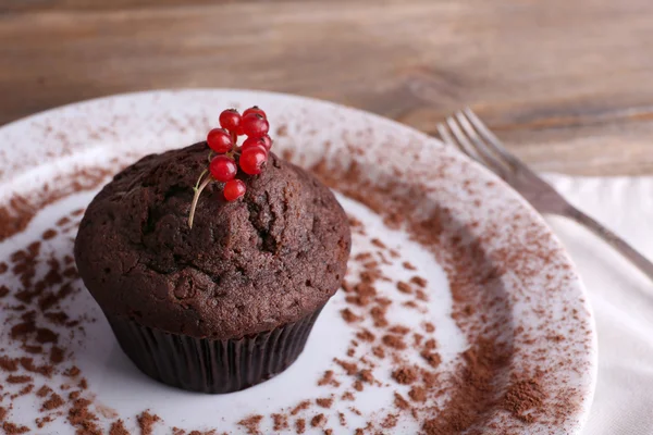 Chocolate muffin with red currant on plate on wooden background — Stock Photo, Image