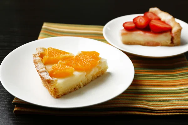 Шматок домашніх апельсинових і полуничних пирогів на тарілці, на кольоровому дерев'яному фоні — стокове фото
