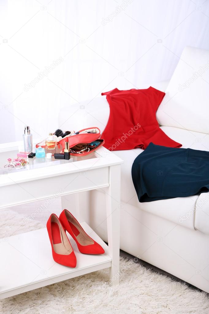 Cosmetic bag, fashion clothes, bottle of perfumes on sofa on light background