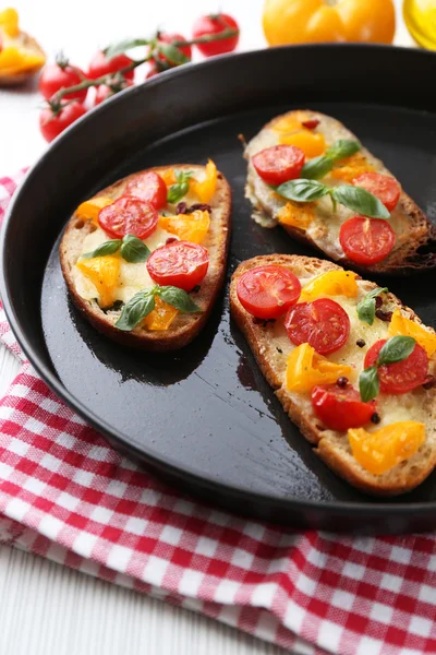 Tasty bruschetta with tomatoes in pan, on table — Stock Photo, Image