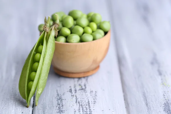 Green peas in wooden bowl on wooden background — Stock Photo, Image