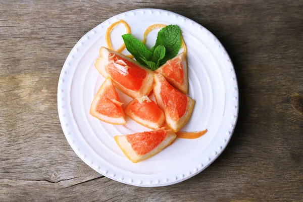 Стиглі подрібнені грейпфрути з листя м'яти на тарілці, на дерев'яному фоні — стокове фото