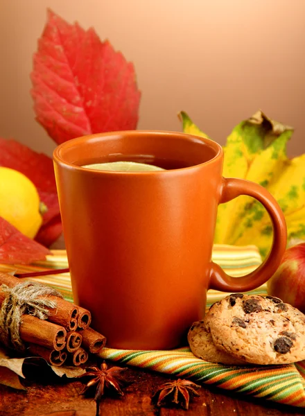 Cup of hot tea and autumn leaves, on brown background — Stock Photo, Image
