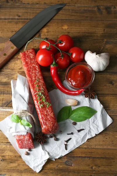 Tasty salami sausage and spices on wooden background — Stock Photo, Image