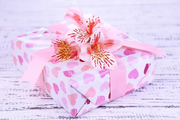 Rosa gåva med båge och blomma på träbord närbild — Stockfoto