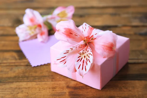 Presente rosa com arco e flor na mesa de madeira close-up — Fotografia de Stock