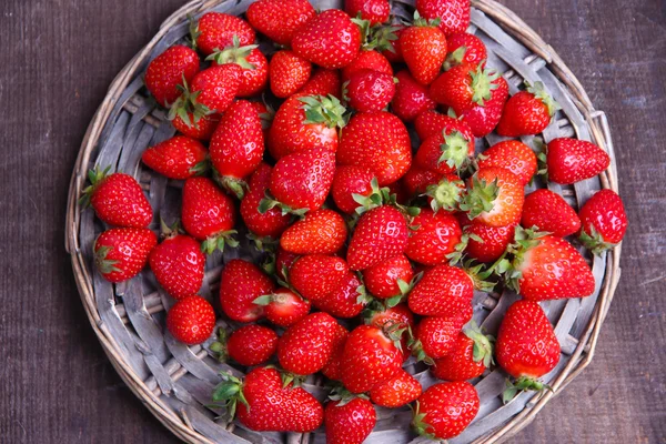 Maturare dolci fragole su stuoia di vimini, su sfondo di legno a colori — Foto Stock