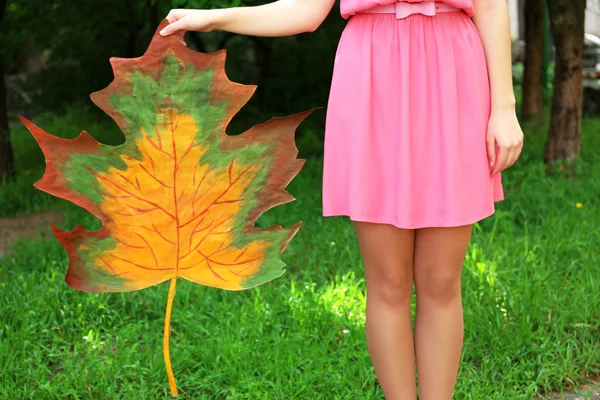 Девушка держит в парке декоративный кленовый лист — стоковое фото