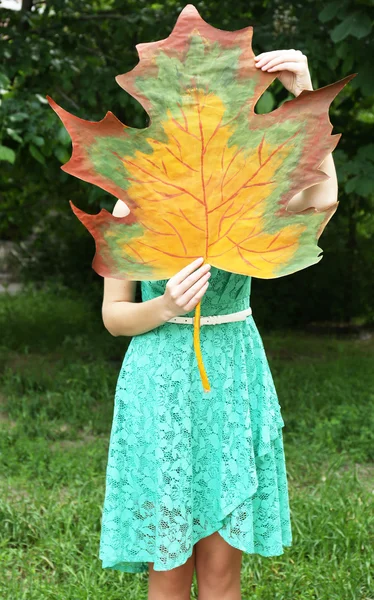 Girl holding decorative maple leaf in park — Stock Photo, Image