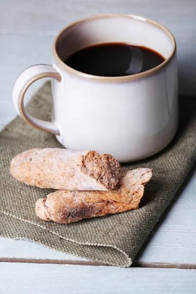 Taza con café caliente y granos de café tostados en servilleta, sobre fondo de mesa de madera — Foto de Stock