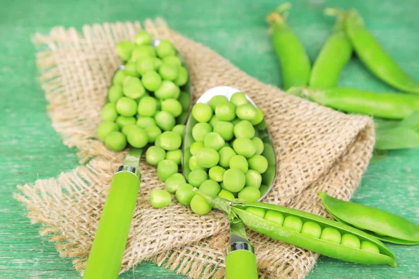 Frische grüne Erbsen in Löffeln auf Holztisch — Stockfoto