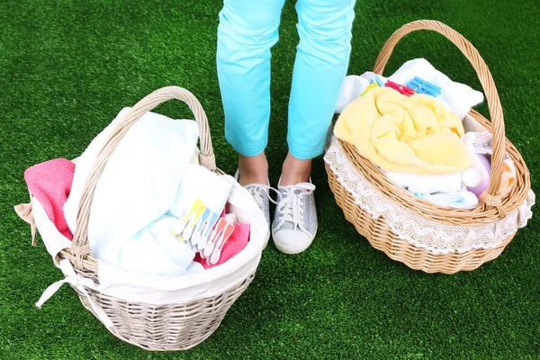 Mulher segurando cestas de roupa com roupas limpas, toalhas e pinos, no fundo grama verde — Fotografia de Stock