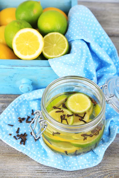 Pickled limes and cloves in glass jar, on color wooden background — Stock Photo, Image