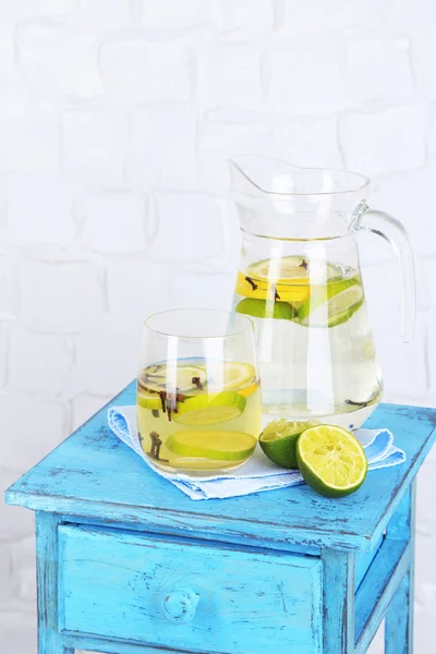 Fresh summer drink with lime and cloves in glass and jug, on color wooden stand, on light wall background — Stock Photo, Image