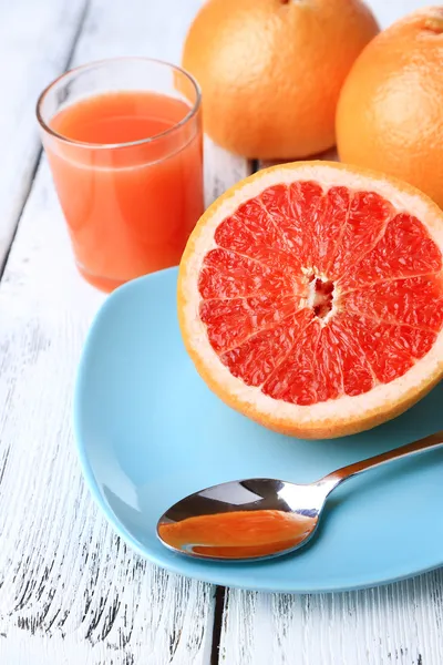 De helft van grapefruit, glas vers sap en lepel op plaat op lichte achtergrond — Stockfoto
