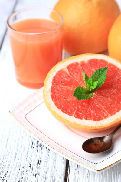 Hälfte Grapefruit, Glas mit frischem Saft und Löffel auf Teller auf hellem Hintergrund — Stockfoto