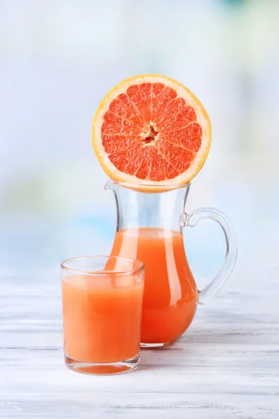 Grapefruit juice in glass and jug on color wooden background — Stock Photo, Image