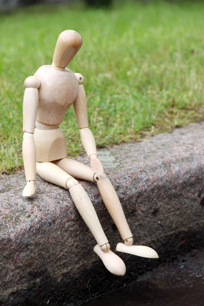 Деревянная кукла сидит на камне, на открытом воздухе — стоковое фото