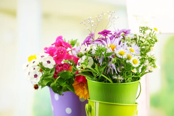 Bouquet of colorful flowers in decorative buckets, on chair, on bright background — Stock Photo, Image