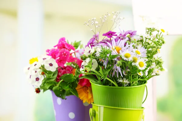 Buquê de flores coloridas em baldes decorativos, na cadeira, no fundo brilhante — Fotografia de Stock