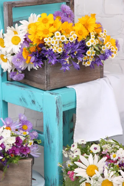 Beautiful flowers in crates on small chair on light background — Stock Photo, Image