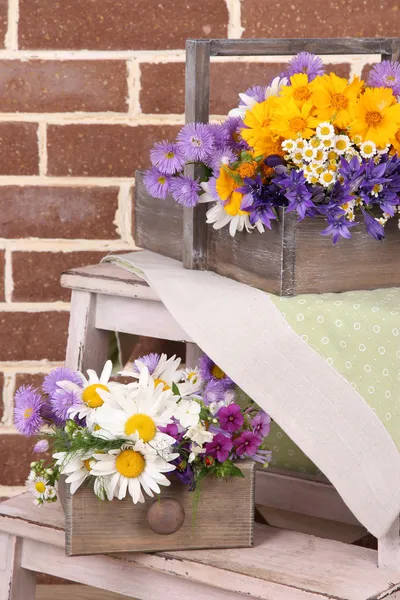 Beautiful flowers in crates on small ladder on brick wall background — Stock Photo, Image