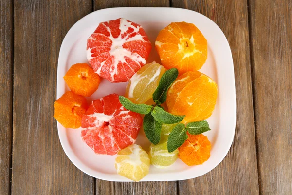 Citrus fruits without skin, on plate, on wooden background — Stock Photo, Image