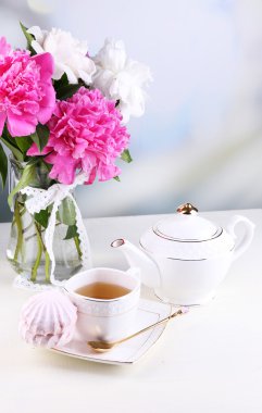 Cam vazo içinde sunulan güzel peonies, çay Kupası ve hatmi, masada açık renkli üzerinde kompozisyon