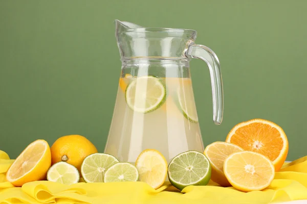 Цитрусовый лимонад в стеклянном кувшине цитрусовых вокруг на желтой ткани на зеленом фоне — стоковое фото