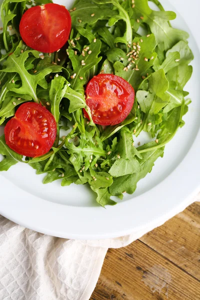 Salada verde feita com arugula, tomates e gergelim na placa, no fundo de madeira — Fotografia de Stock