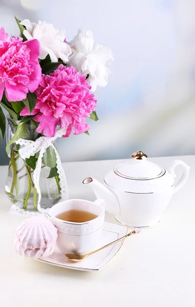 Samenstelling van prachtige pioenrozen in vaas, thee in cup en marshmallow, op tafel, op lichte achtergrond — Stockfoto