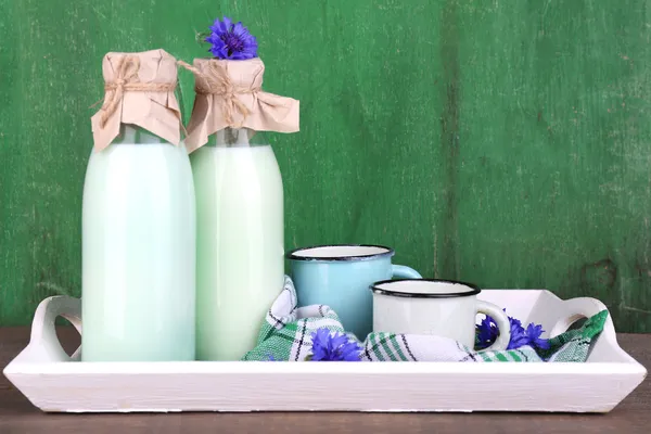 Bottiglie e tazze di latte con fiordaliso su vassoio di legno — Foto Stock