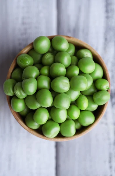 Green peas in wooden bowl on wooden background