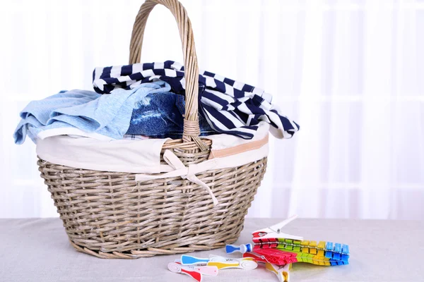 Colorful clothes in basket and pins on table, on light background — Stock Photo, Image
