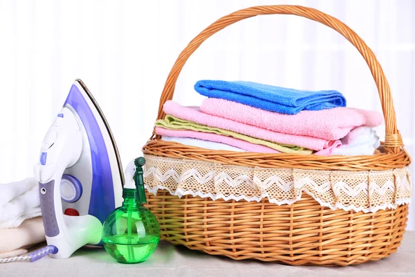 Colorful towels in basket, iron on light background — Stock Photo, Image