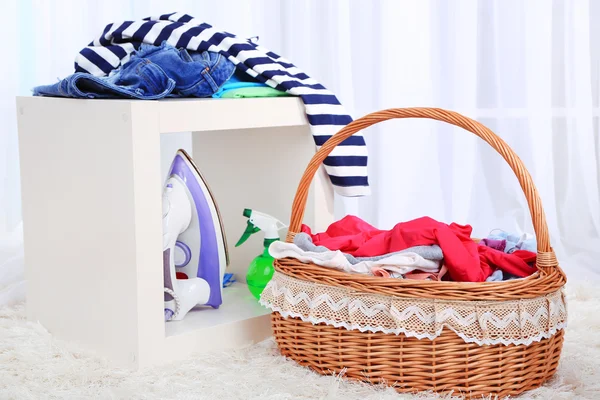 Colorful clothes in basket on chair, on light background — Stock Photo, Image