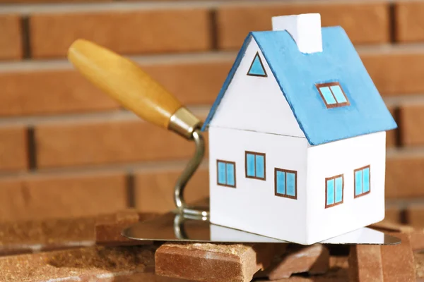 Wooden toy house on trowel and tiles on brick wall background — Stock Photo, Image