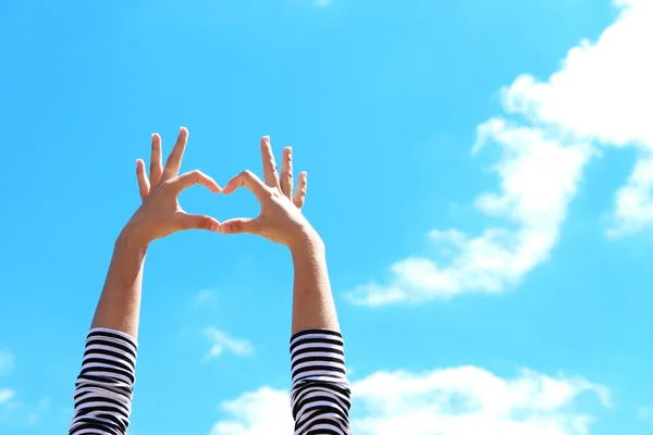 Young girl holding hands in heart shape framing on blue sky background — Stock Photo, Image