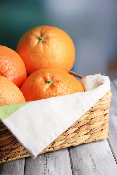 Спелые грейпфруты в плетеной корзине на деревянном столе, на ярком фоне — стоковое фото