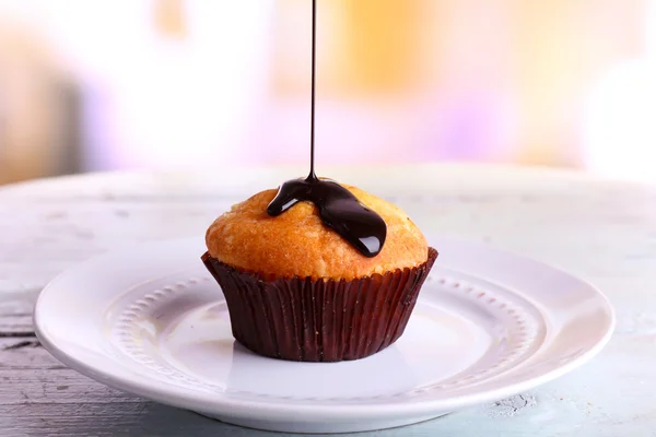 Smaczne muffin z czekoladowym sosem na talerzu, na jasnym tle — Zdjęcie stockowe