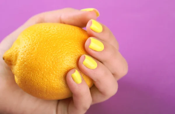 Mão feminina com unhas coloridas elegantes segurando limão fresco, em fundo de cor — Fotografia de Stock