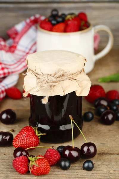 Smakelijke jam met bessen in glazen pot op houten tafel — Stockfoto