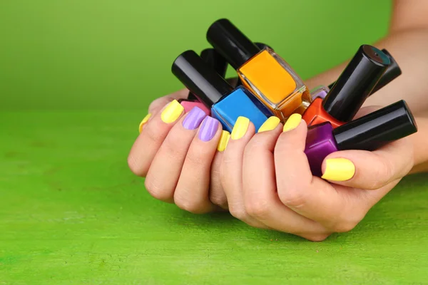 Manos femeninas con elegantes uñas de colores sosteniendo botellas con esmalte de uñas, sobre fondo verde — Foto de Stock