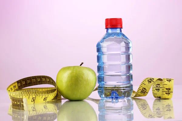 Botella de agua, manzana y cinta métrica sobre fondo púrpura — Foto de Stock