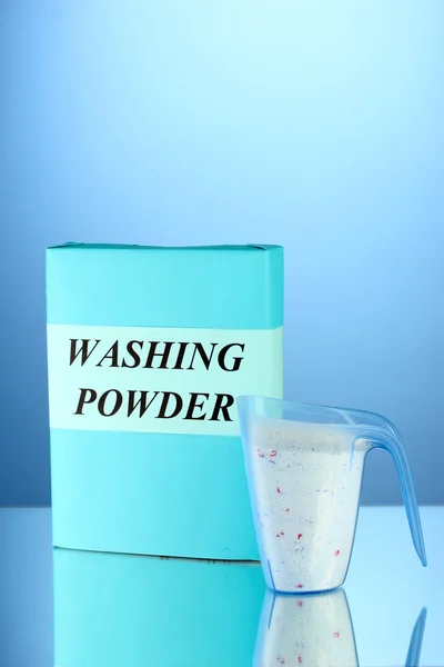 Box of washing powder with blue measuring cup, on blue background close-up — Stock Photo, Image
