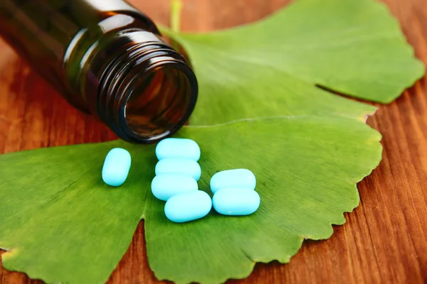 Ginkgo biloba leaves and medicine bottle on wooden background — Stock Photo, Image